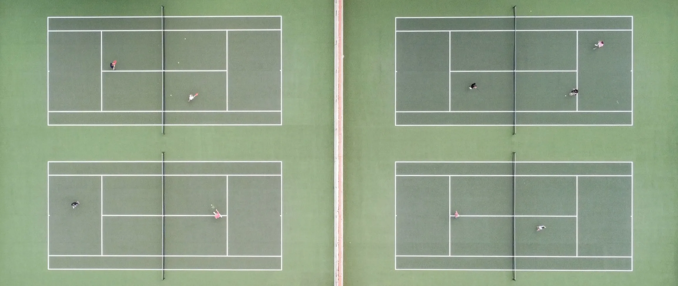 Four tennis courts seen from directly above, with games in play on each
